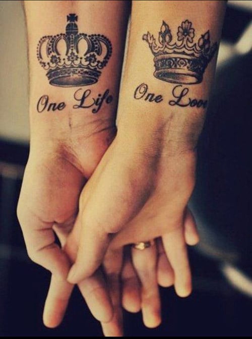 manos de una pareja entrelazadas mostrando su tatuaje en forma de coronas 