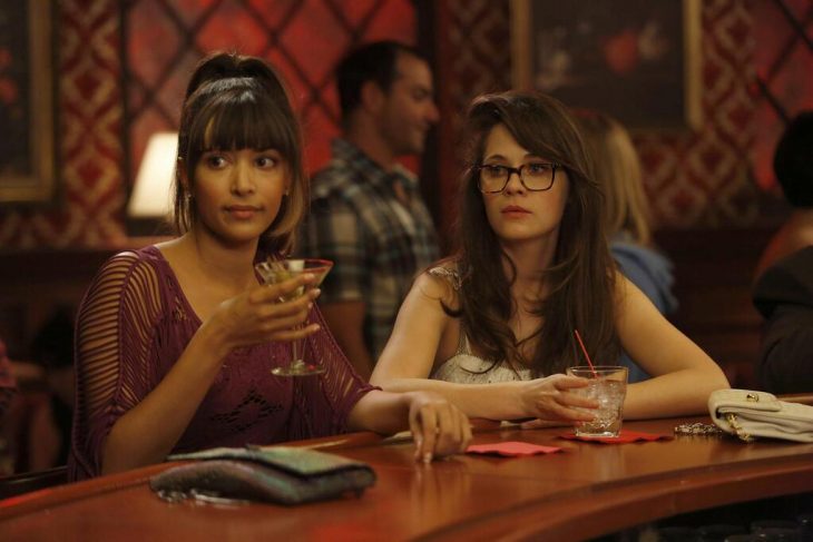 cece and jess de new girl bebiendo sentadas en la barra de un bar 