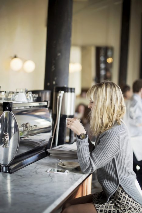 chica en una barra tomando café sola 