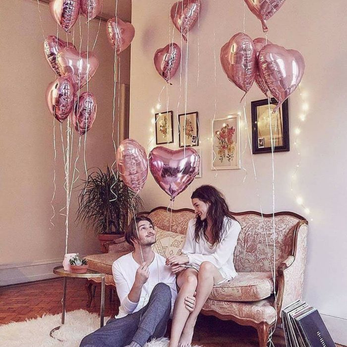 Pareja en sala de una casa con globos en forma de corazón