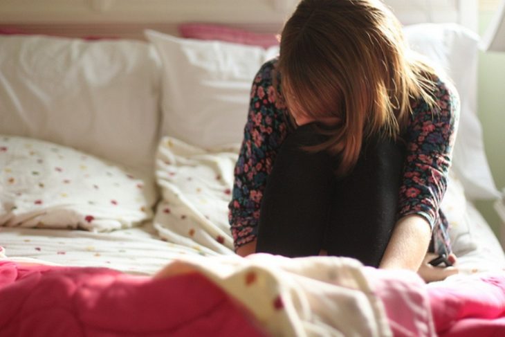 Chica triste sentada en la cama 