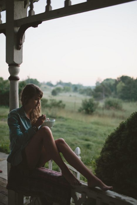 chica sentada en el balcon comiendo un tazón de cereal 