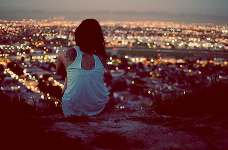 chica sentada en una roca viendo la ciudad 
