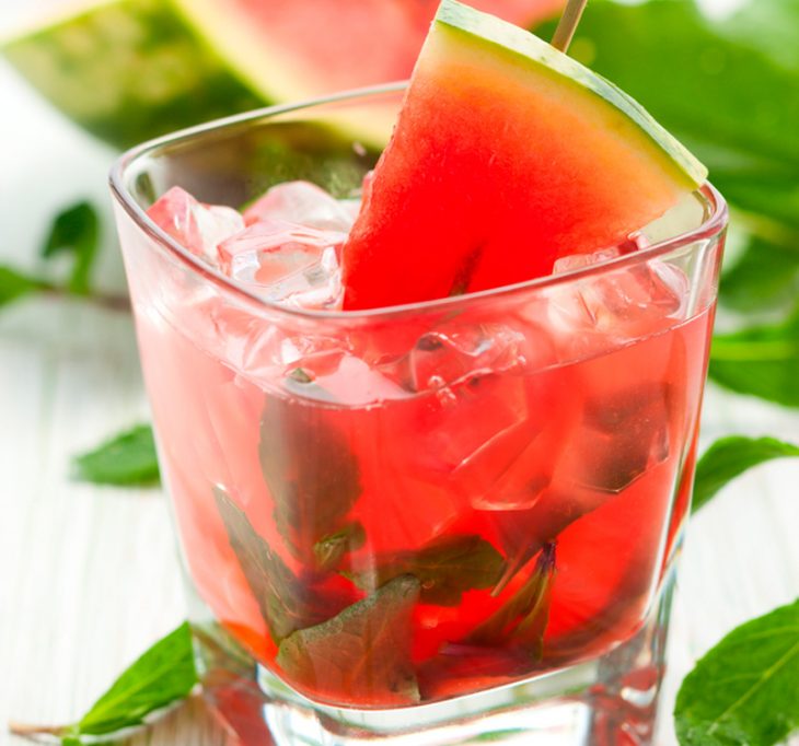 vaso con agua de sandia y mentas esparcidas en una mesa 