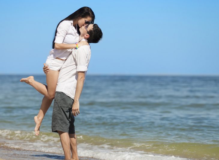 novio cargando a su novia y besándola en la playa 