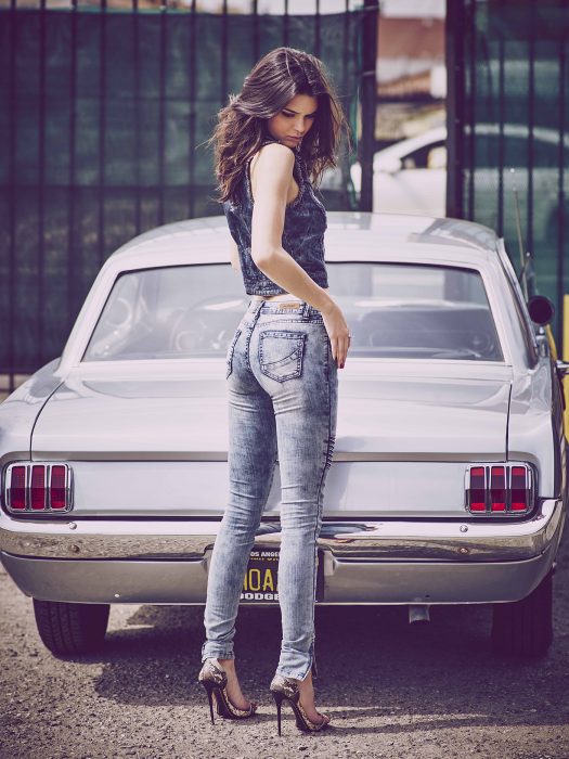 chica recargada de frente en un carro usando pantalón y chaleco de mezclilla 