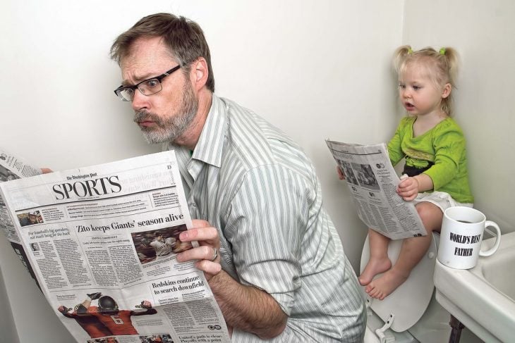 hombre sentado en el baño leyendo el periódico 