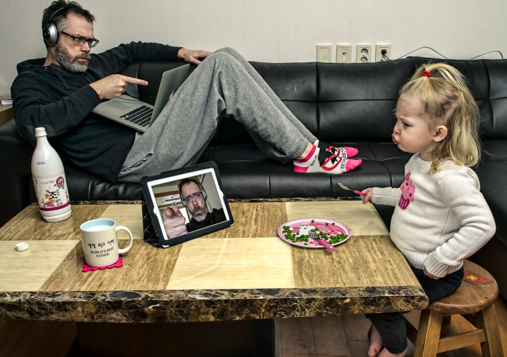 hombre con una computadora en los pies mientras una niña ve una tablet en una mesa 