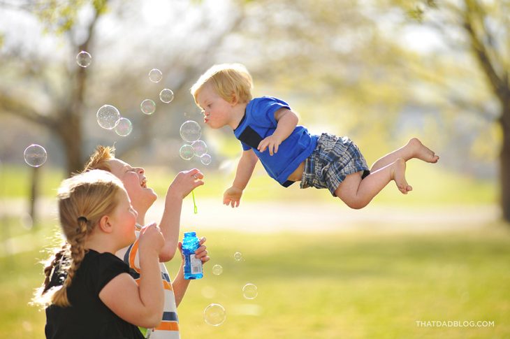 niño que simula volar sobre las personas mientras hace bombas de jabón 