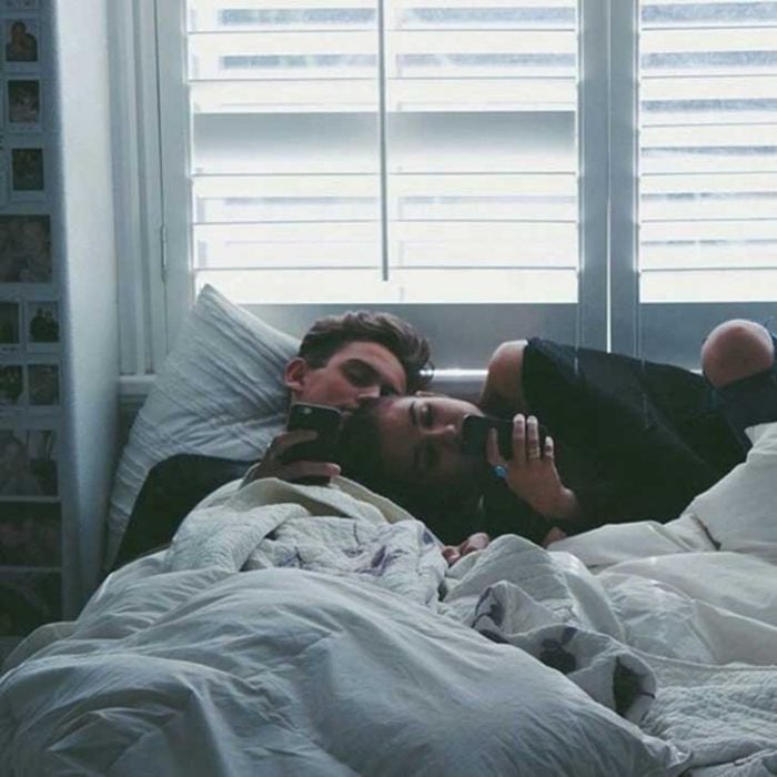 pareja recostada en la cama viendo su celular 
