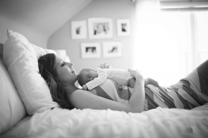 mujer recostada en una cama con un bebé sobre su pecho 