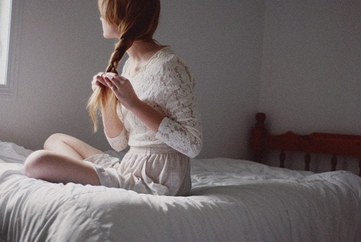 chica sentada en una cama haciéndose una trenza en el cabello 