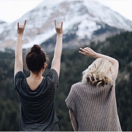 chicas sentadas viendo una montaña y levantando los brazos 
