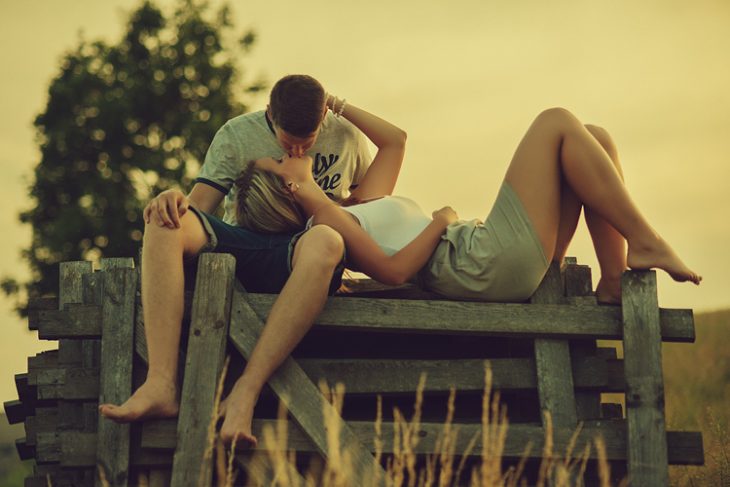 pareja de novios sentados en un muelle besándose y acariciándose 
