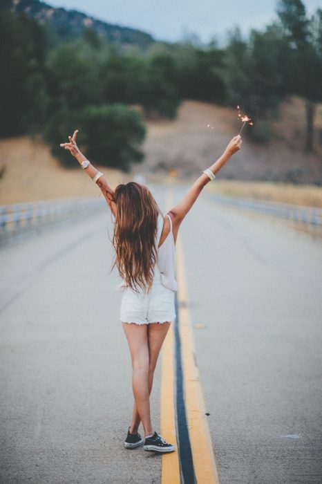 chica en una carretera levantando las manos 