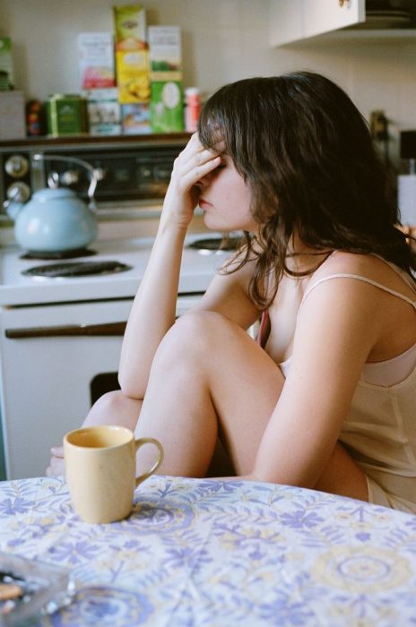 Chica tocándose la cabeza mientras toma café 