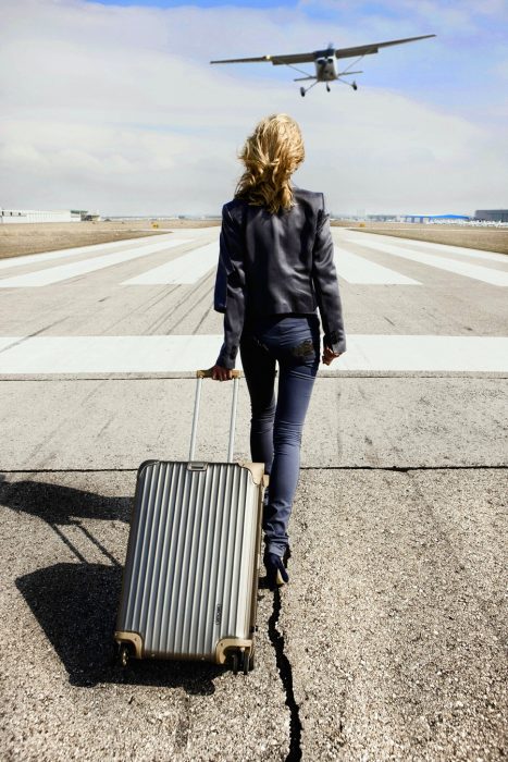 Chica con una maleta en una pista de aterrizaje 