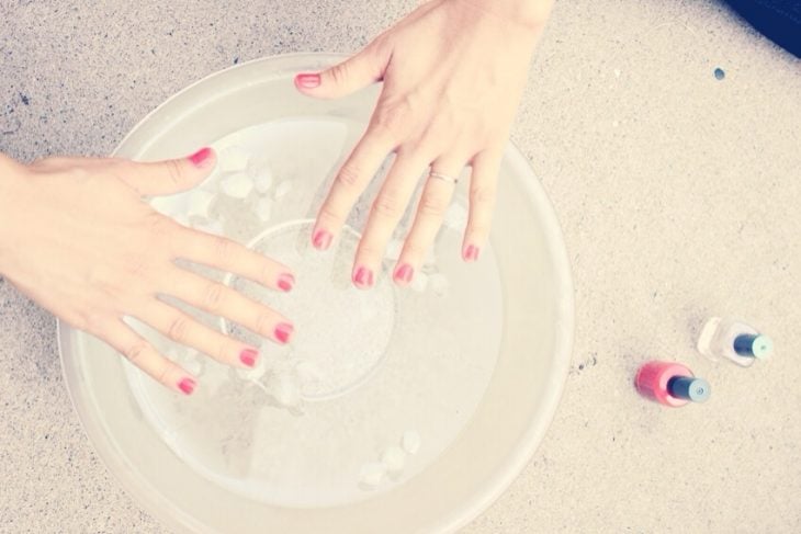 Uñas recién pintadas sumergidas en agua con hielos