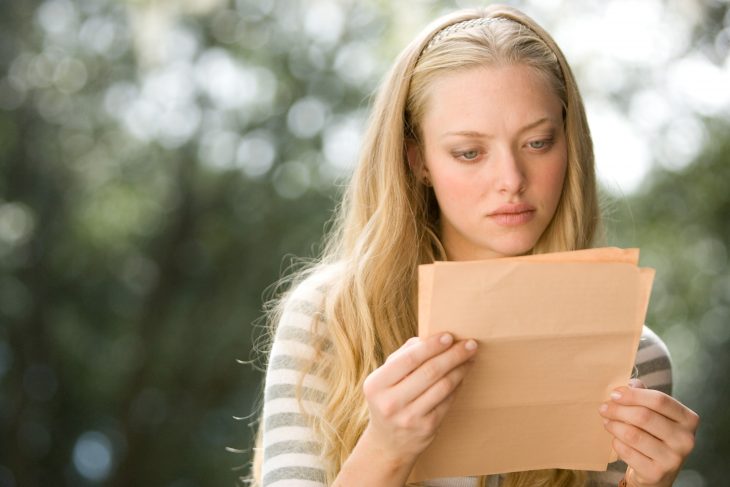 chica rubia leyendo una carta con cara de preocupación 