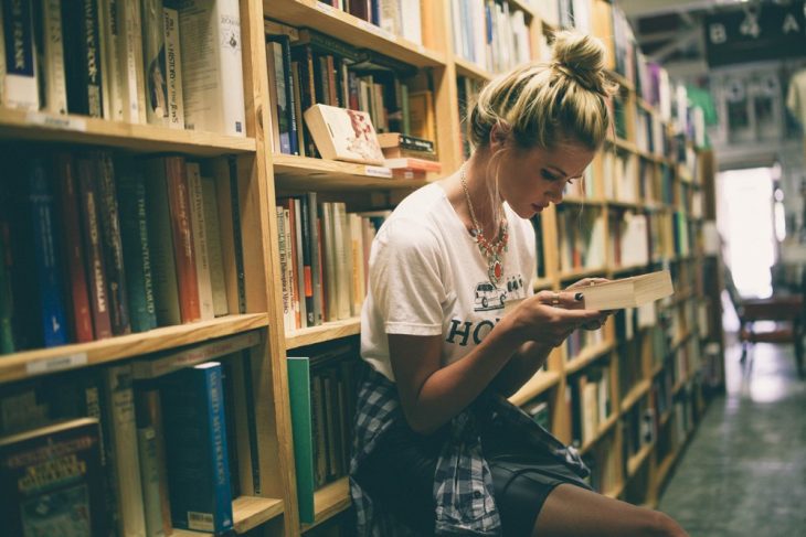 chica en una biblioteca leyendo un libro 