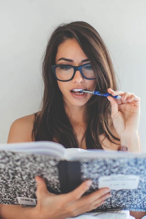 chica con una libreta en sus manos mordiendo un lápiz 