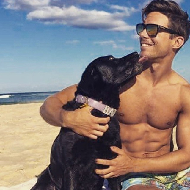 chico en la playa sentado junto a su perro mientras este le da un beso con su lengua 