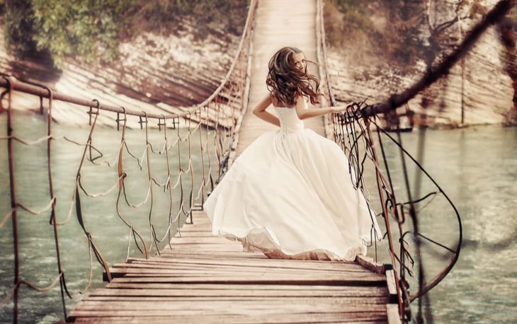 chica en vestido de novia corriendo sobre un puente