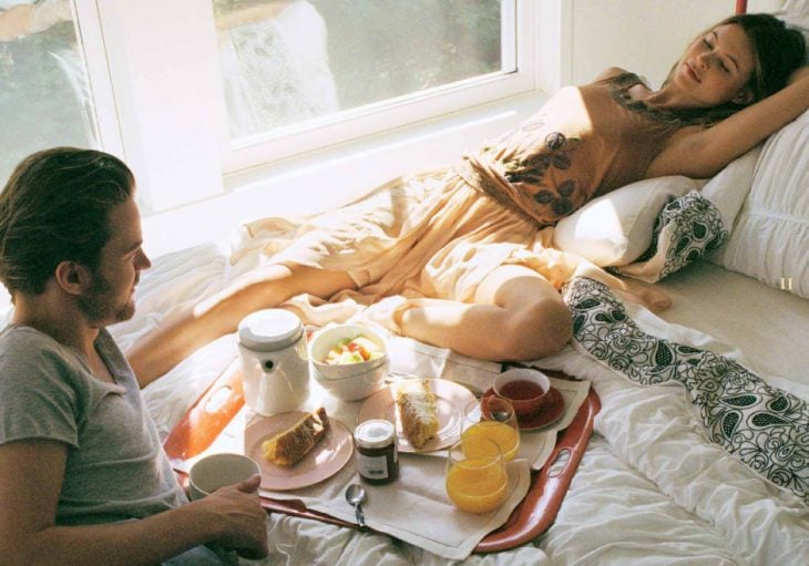 pareja de novios recostados en la cama listos para desayunar 