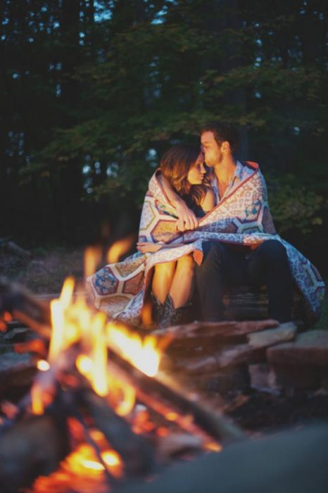 pareja de novios frente a una fogata abrazados y besándose 