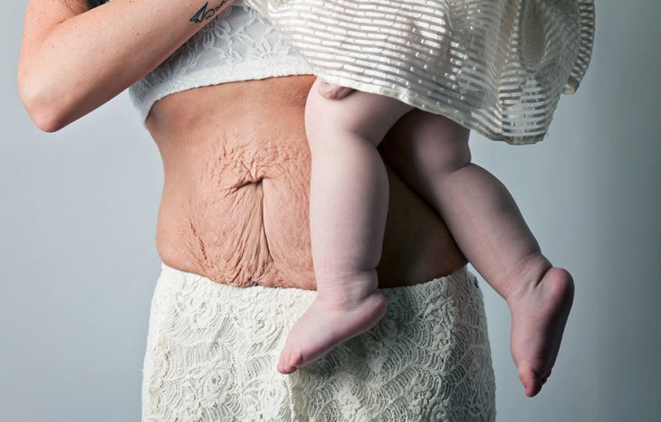 mujer cargando a un bebé en brazos y mostrando su abdomen 