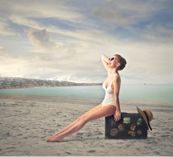 Chica sentada sobre un maleta en la playa 