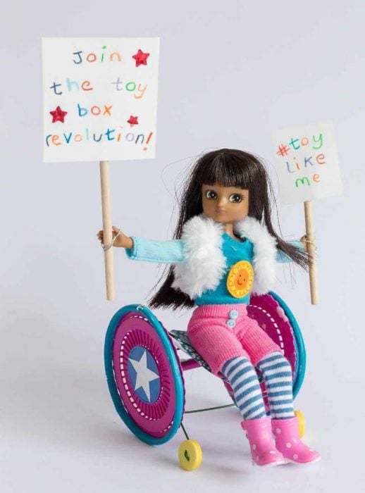 Muñeca que esta sentada en una silla de ruedas con carteles de propuesta 