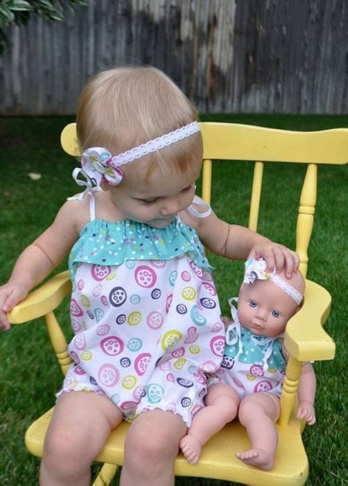 niña sentada en una silla junto a su muñeca vestidas de la misma manera 