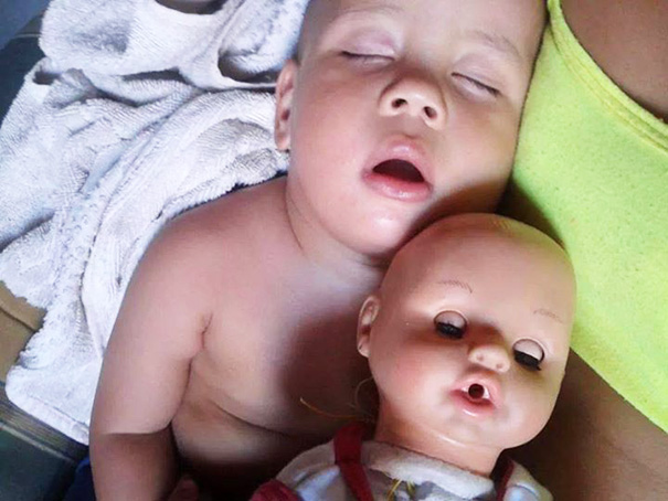 bebé recostado junto a su muñeco que también tiene la boca entre abierta 