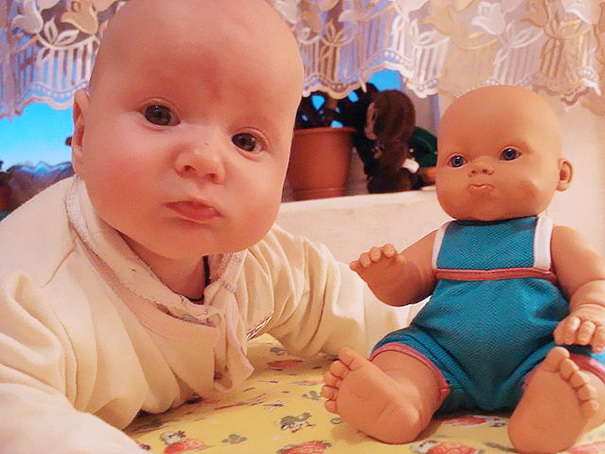 bebe que es idéntico a su muñeca, ambos se encuentran en la cama recostados 