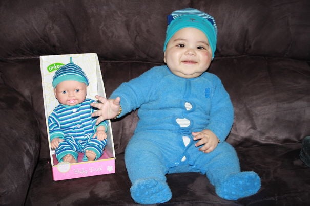 bebé sentado junto a un muñeco que tiene un mameluco de color azul que es igual a él