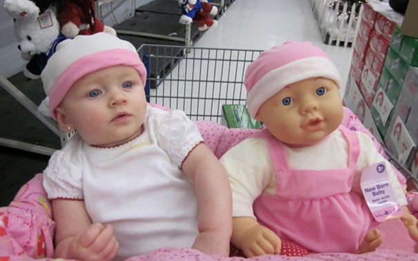 bebe sentado en un carrito de super mercado junto a su muñeca que se parece a ella