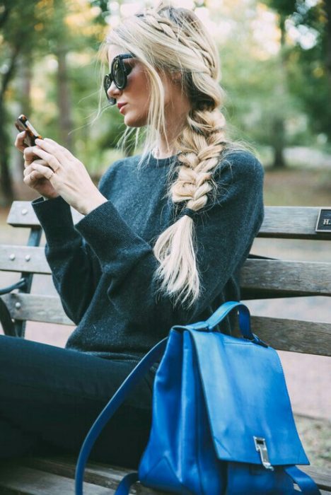 chica observando su celular en una banca del parque 