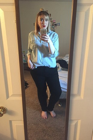 chica rubia usando una blusa de mezclilla y pantalón negro tomándose una foto frente al espejo de su cuarto 