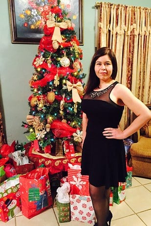 mujer usando un vestido negro parada junto a un árbol de navidad 