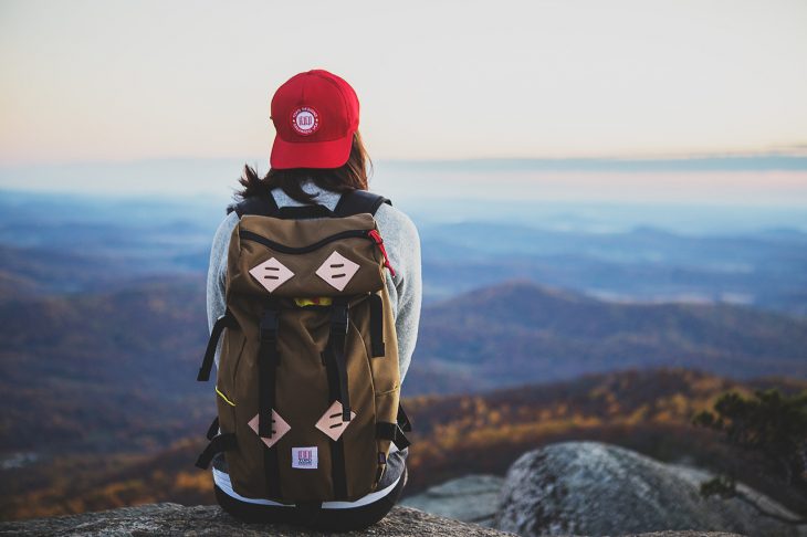 chica sentada en una montaña con una mochila de viaje en su espalda