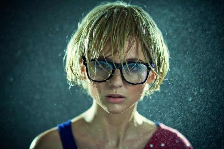 chica rubia usando lentes y parada bajo la lluvia 