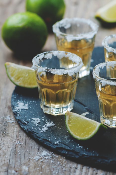 shots de tequila puestos en una mesa junto con limones y sal