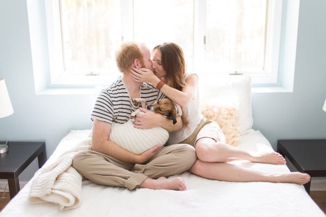 pareja de novios sentados en una cama besándose y sosteniendo a su perro 