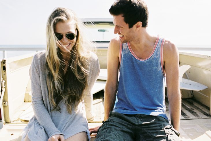 Chica sonriendo junto a un chico mientras están sentados en una barca 