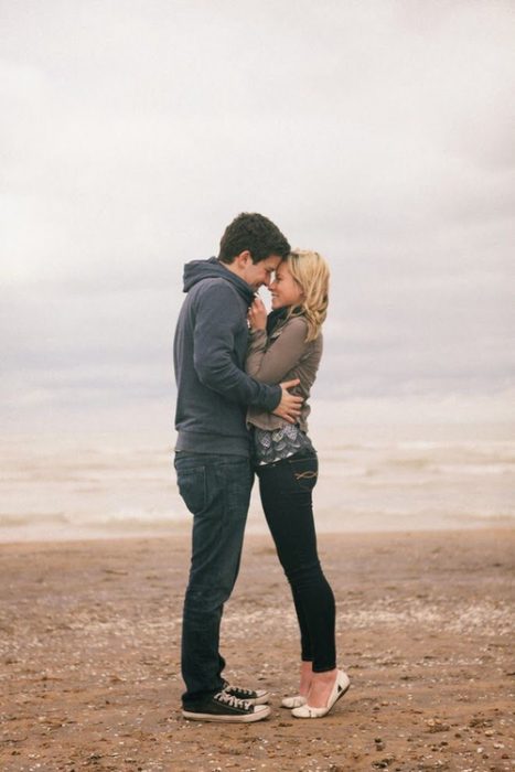 Pareja de novios abrazados mientras estan parados en una playa viendo el mar