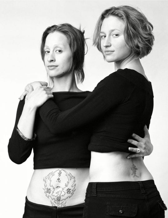 mujeres abrazadas con tatuajes que parecen gemelas 