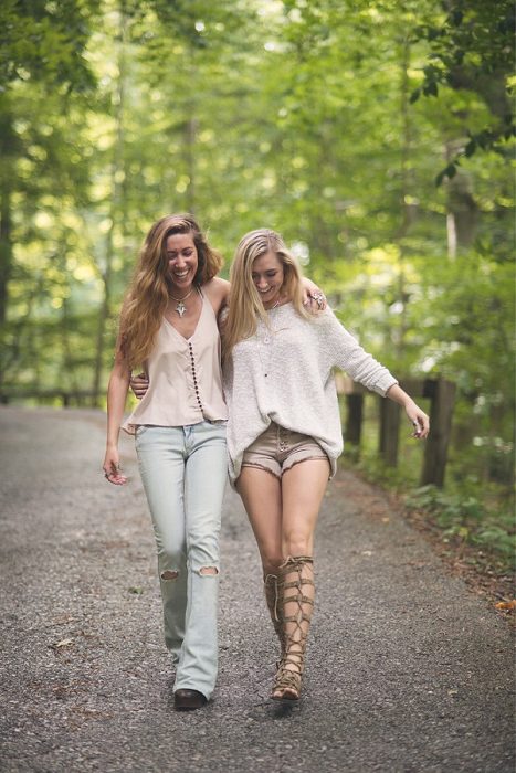 Chicas abraadas caminando por la carretera rodeadas de árboles mientras están abrazadas 