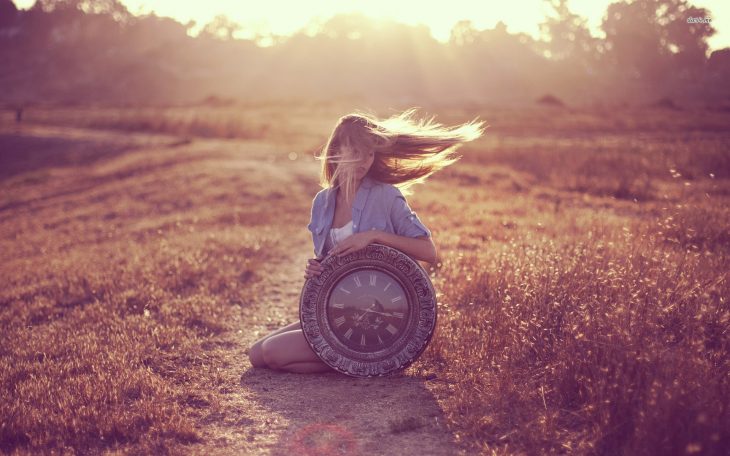 Chica sosteniendo un reloj grande mientras esta sentada en la hierba 