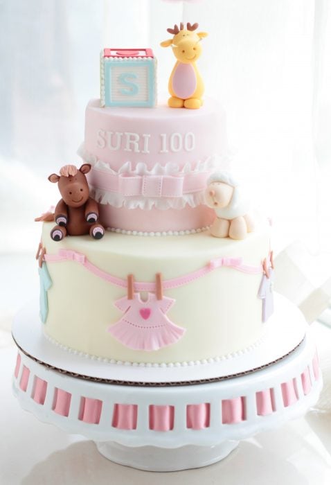 pastel de baby shower para niña de color rosa y blanco y decoraciones de osos y ropita 
